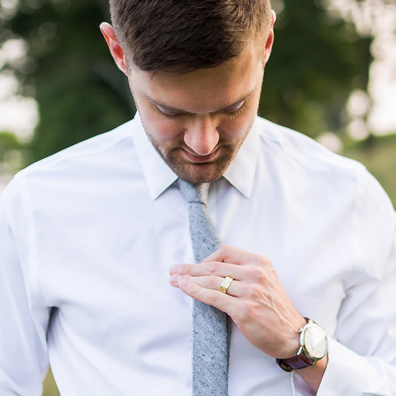 Man wearing dress shirt and tie looking down at wedding band on his finger