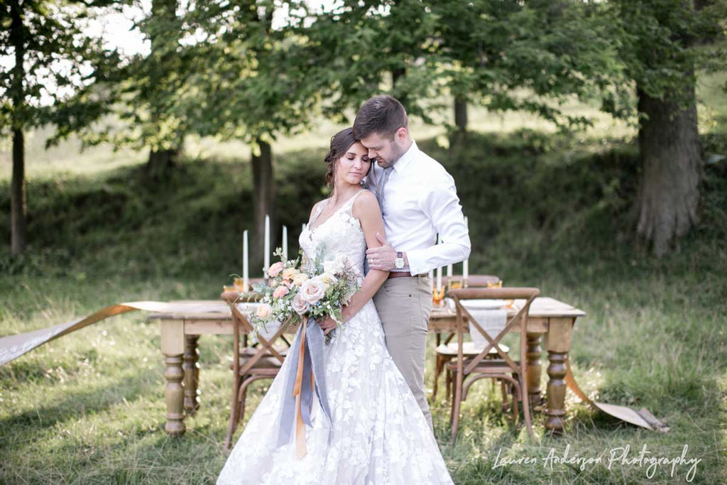 Photo of newlywed couple standing in a field with a wooden table behind them