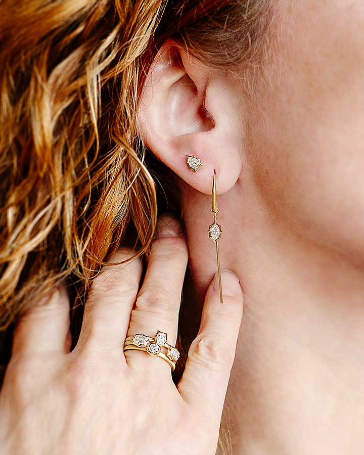 Hand wearing ring held up to neck underneath ear with earring on it