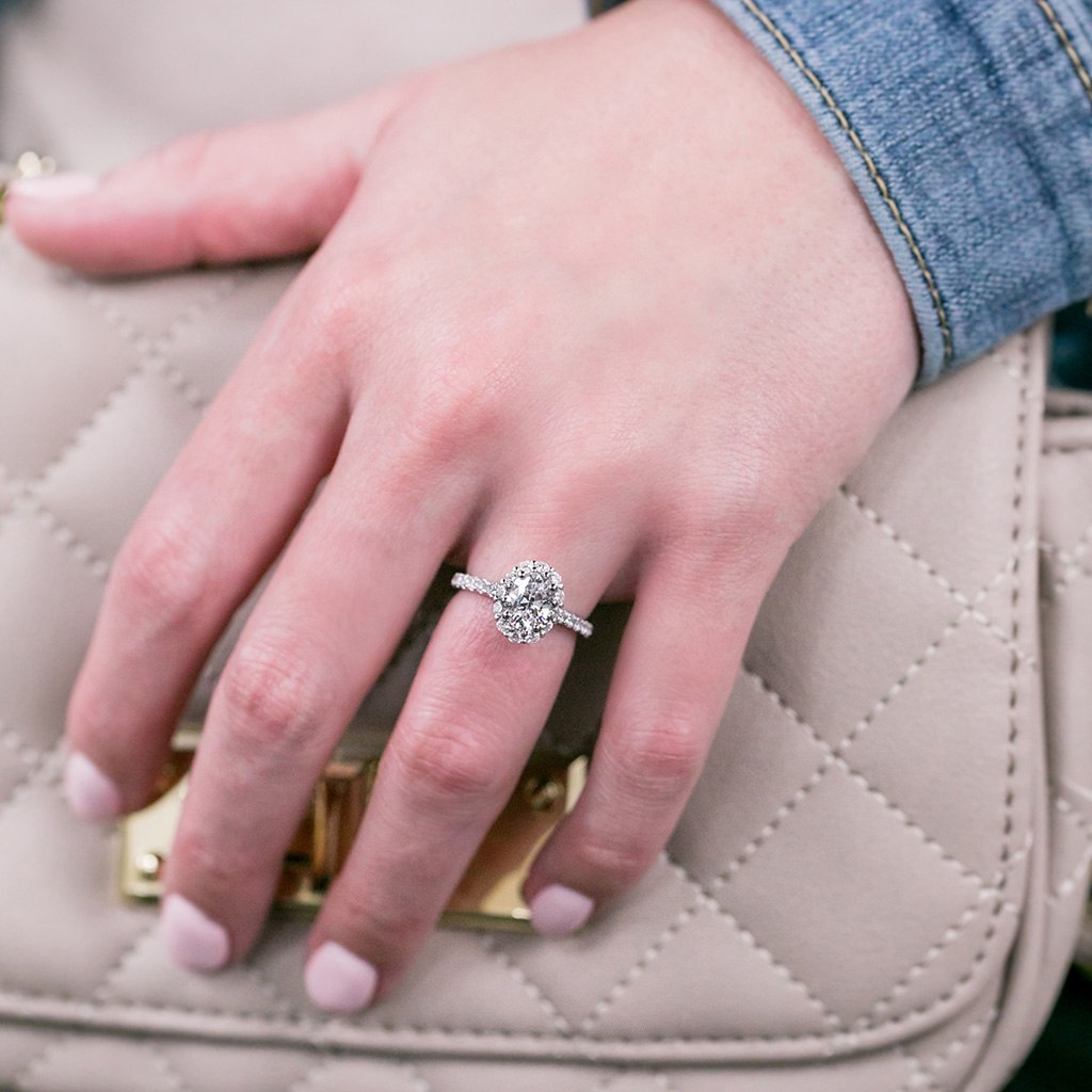 Hand with diamond engagement ring resting in front of handbag